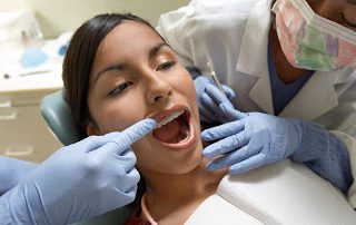 Photo of a young woman having her teeth examined by an orthodontist for invisalign vs. braces treatment options.