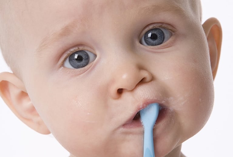 Photo of an infant with blue eyes and a blue toothbrush in their mouth, illustrating care for baby teeth.
